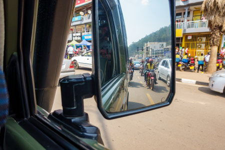 Kigali Rwanda - September 9 2025; Urban street scene with surrounding street and buildings and taxi moto reflected in rear vision mirror.のeditorial素材