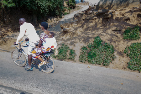 Kigali Rwanda - September 9 2025; Family of three on one bicycle in hot day with man pedaling taking all three to destination.のeditorial素材