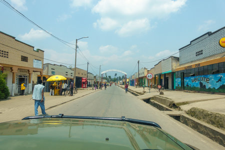 Kinigi Rwanda - September 8 2025; View through windscreen looking at road ahead with arched sign for Model Village of Kinigi lined by buildings with people walking along.のeditorial素材
