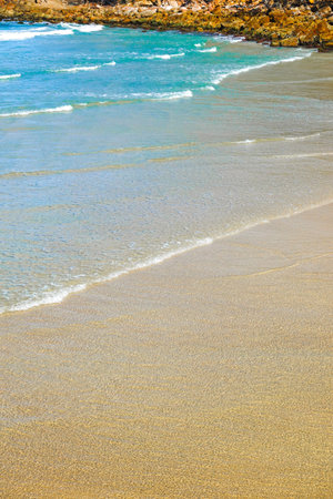 Low ocean waves washing on shore of sand and turquoise sea on tropical beach in vertical...