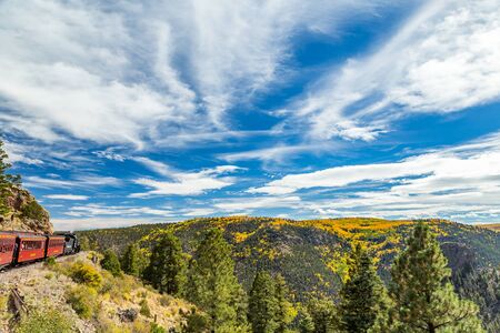 a cumbres & Toltec steam locomotive heads up a mountain side with a passenger train while traveling through the San Juan National Forest on a trip from Chama, New Mexico through a beautiful scenic route ending in Antonito, Coloradoのeditorial素材