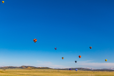 With the Colorado Rocky Mountains as a backdrop, hot air balloons take advantage of a clear early morning and an open rural field to practice taking off and touching down.のeditorial素材