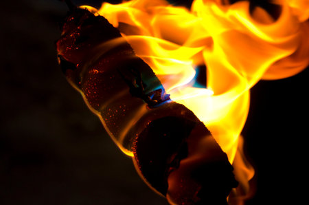 A hot dog on fire with a close up few of the flames burning away in the dark night.