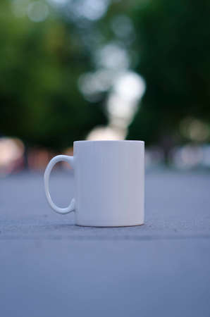 A solo blank white coffee mug on the sidewalk of the park in the summer evening sun.の写真素材
