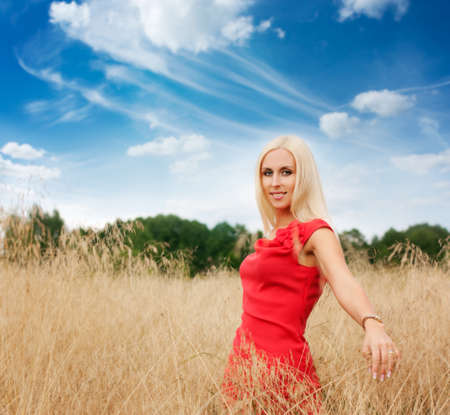 Smiling Blonde Woman in Red Dress Standing in the Fieldの写真素材