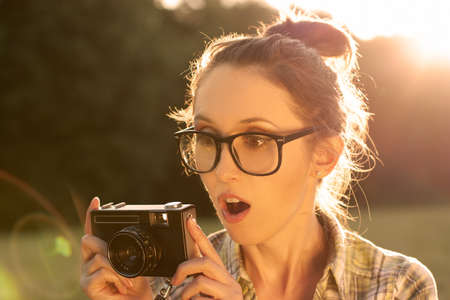 Surprised Hipster Girl in Glasses Taking a Photo with Vintage Cameraの写真素材