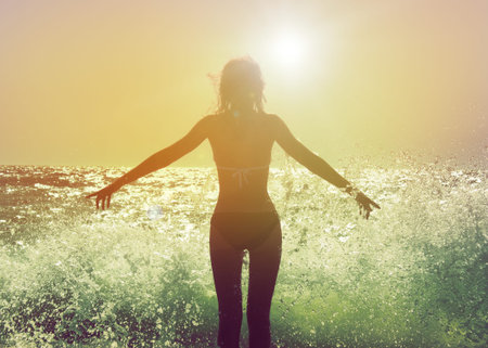 Beautiful Woman in Bikini Standing in the Sea Waves and Enjoying Sunshine with Open Armsの写真素材