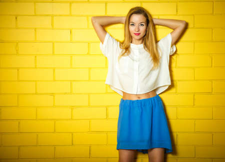 Portrait of Trendy Hipster Girl with Hands behind Head on Yellow Brick Wall Background. Urban Fashion Concept. Copy Space.の写真素材