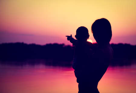 Silhouettes of Father and Baby Watching Sunset by the Lake.  Family Concept. Toned Photo with Copy Space.の写真素材