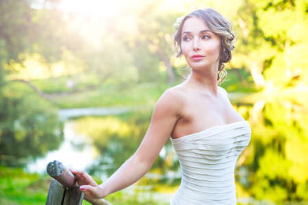 Stylish Young Bride Outdoors Portrait at Green Nature Background. Modern Wedding Hairstyle and Accessories. Sunset Light. Toned Photo with Copy Space.の写真素材
