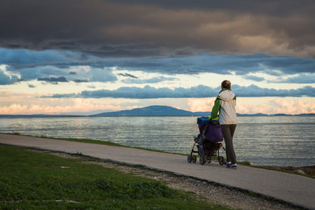 Mother with Baby Stroller Walking by the Sea and Enjoying Beautiful Seascape in Evening. Happy...