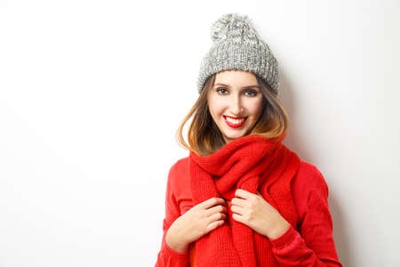 Smiling Girl in Red Sweater, Scarf and Beanie Hat on White Background. Portrait Not Isolated. Winter Fashion Concept.の写真素材