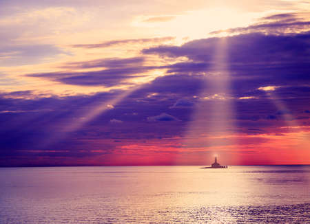Lighthouse at Sunset. Beautiful Sea and Dramatic Sky Clouds Background with Sunrays. Nautical Concept. Toned Photo with Copy Space.の写真素材
