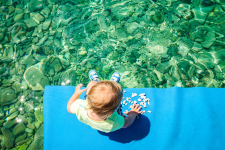 Baby Playing with Stones by the Sea. Top View. Crystal Clear Azure Water of Adriatic Sea Background....