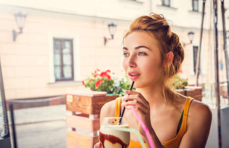 Young Fashion Woman Drinking Ice Coffee in a Cafe Outdoors in the City. Toned Instagram Styled Photo with Copy Space.の写真素材