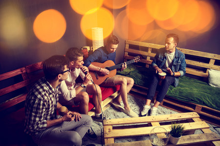 Group of Four Friends Hanging Out in Studio. Guys Singing and Playing Music in Urban Apartment....