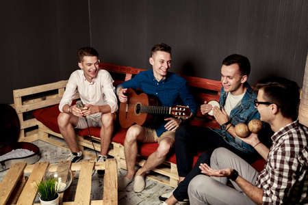 Group of Happy Smiling Four Friends Hanging Out in Studio. Guys Singing and Playing Music in Urban Apartment. Toned Photo with Bokeh.の写真素材