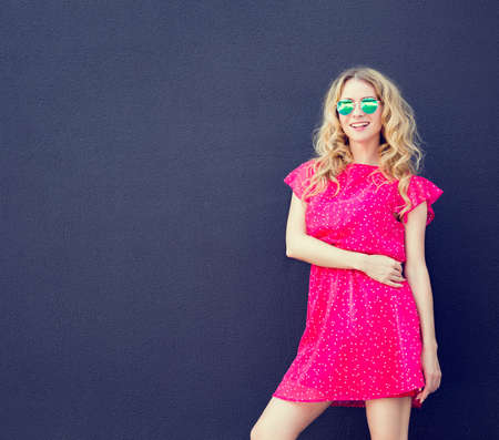 Fashion Woman in Pink Dress and Sunglasses at the Dark Textured Wall Background. Urban Fashion Girl in Summer Concept. Street Style Female. Toned Photo with Copyspace.の写真素材
