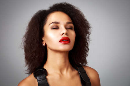 Portrait of Dreaming Fashion Woman in Black Dress on Gray Background. Beautiful Mixed Race Girl Close Her Eyes. Female with Curly Hair and Red Lipstick. Toned Photo with Copy Space.の写真素材