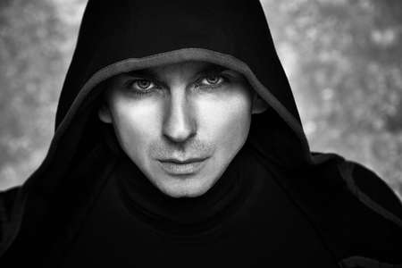 Mysterious Man in Black Hoodie. Sexy Hero Guy. Pastor or Wizard in Robe. Assassin or Witcher with Strong Face Expression in Cloak. Dark Magician Black and White Photo. Fantasy Book Cover Concept.の写真素材