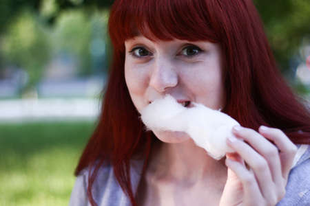 Cute girl is eating pink candyfloss with joy in bright summer in nature green backgroundの写真素材