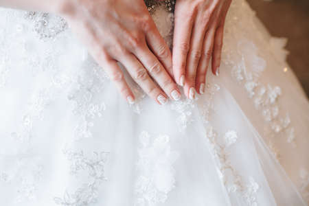 Hands bride with a manicure on the background of white lace dressの写真素材