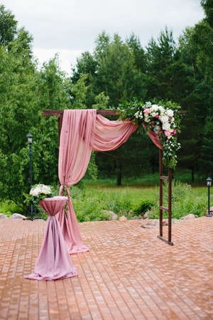 Arch for the wedding ceremony. Arch, decorated with beautiful fresh flowers and cloth. Bordeaux color. Registration at the place of marriage. Wedding arch of real flowersの写真素材
