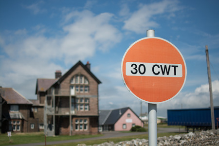 A red road sign, indicating maximum of 30 CWT, hundredweight, with an old abandoned building in the backgroundの写真素材