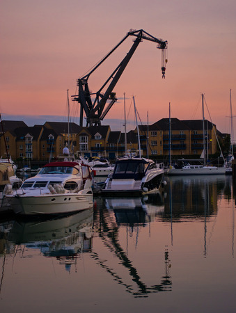 A dockside crane and boats, silhouetted against the setting sunの写真素材