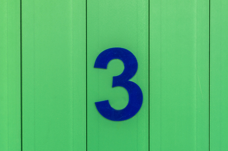 the number three, blue, set against bright green woodの写真素材