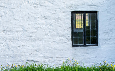 white, stone wall with a black window frame and grass