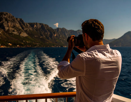 Young man taking photos of mountains and sea from the deck of a cruise shipの素材