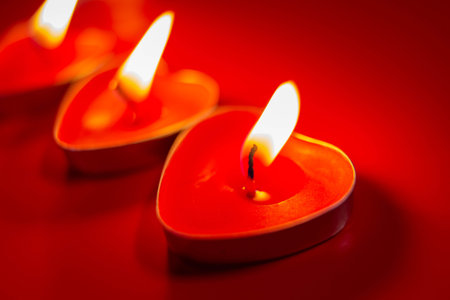 Red burning candles in the shape of a heart with a blazing flame. Tongues of fire on a red background. Valentine's day, passion, love, feelings, romantic mood concept. Decor for February 14th.の写真素材