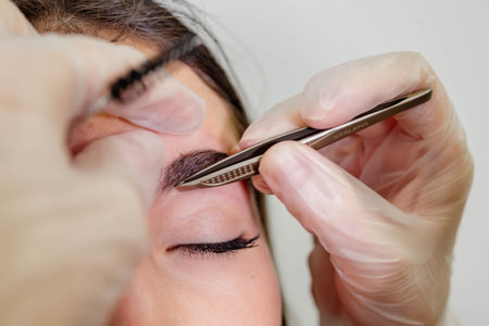 Beautiful young girl with long eyelashes tweezing her eyebrows in a beauty salon. Eyebrow...