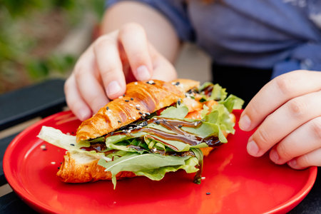 Hand of a woman holding a fresh croissant stuffed with salmon and curd cheese on the summer terrace of a cafe.の写真素材