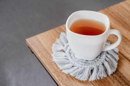 Hobby handmade macrame. Tea in a cup on a gray macrame stand on a wooden table. Eco macrame home decoration.の写真素材