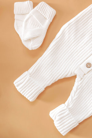 Knitted white jumpsuit for a newborn on a beige background. Outerwear for toddlers for walks in autumn or spring.の写真素材