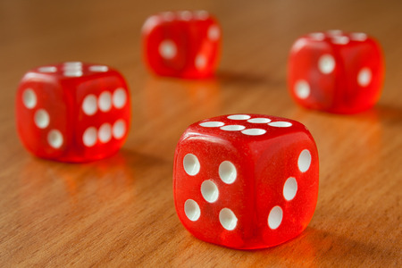 The four red dice lit by sunlight on a wooden tableの写真素材