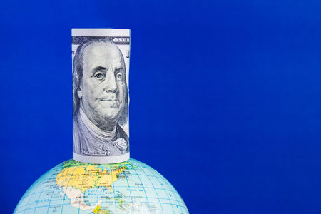 A hundred-dollar bill on top of the globe on a blue background with copy space. Conceptの写真素材