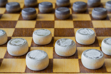 Fragment of wooden checkerboard with checkers spaced on table (closeup)の写真素材