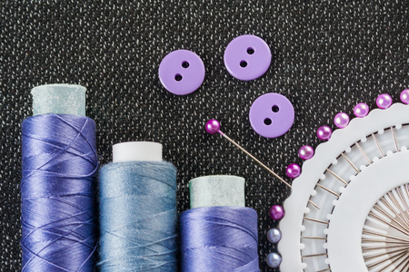 Sewing accessories: spools of threads, needles, buttons, on the textured fabric surface (flat view)の写真素材