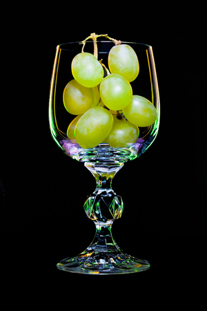 Wine glass filled with branch a grapes on a black background (concept)の写真素材