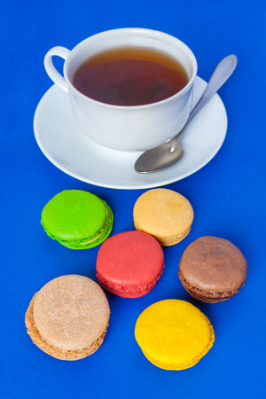 Traditional  french multicolored macarons in the foreground and a cup of tea on a saucer with spoon   on a blue backgroundの写真素材