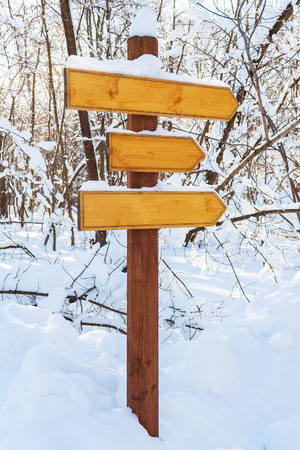 Blank wooden directional arrows on a post, covered by snow in the winter forestの写真素材