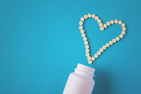 Yellow tablets are laid out in the shape of a heart and white plastic jar on a blue background with copy space (concept, flat lay)の写真素材