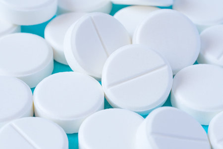 Close up view of a heap of white round pills on a turquoise table as background (macro)
