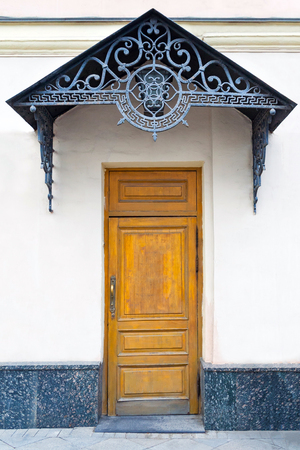 View on a porch with brown wooden door and forged decorative lattice on the pedimentの写真素材