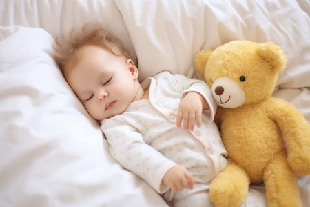 A cute newborn baby sleeping on bed with a teddy bearの素材