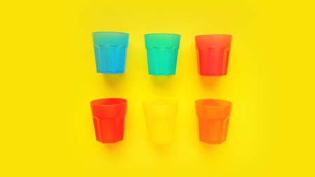 Plastic glass of various color isolated on yellow background - bright summer concept for design and bannersの写真素材