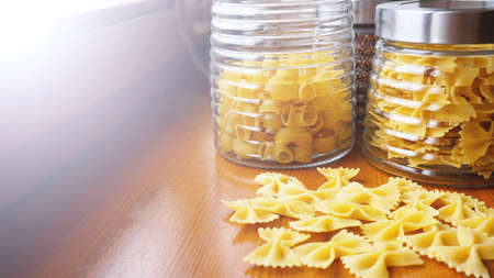 Pasta in the form of bows scattered from glass jar. Italian handmade pasta on the wooden background.の写真素材